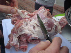 Dad cuts the fat off a piece of lamb meat to prepare it for grinding